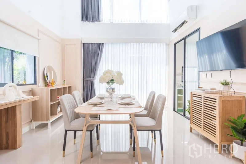 Townhouse for rent or sale in Suan Luang, Bangkok - Bright dining room with double-height ceiling, six-seat table, and sliding door to the kitchen.
