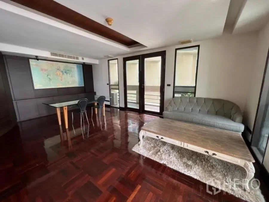 Condominium for rent in Khlong Toei, Bangkok - Multi-purpose family room with parquet floors, balcony access, sofa and glass table.