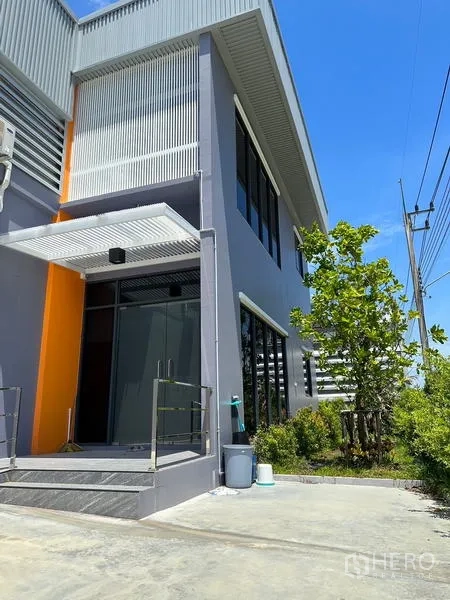 Factory for rent or sale in Lam Luk Ka, Pathum Thani - Front office entrance with glass door, metal canopy and landscaped greenery.