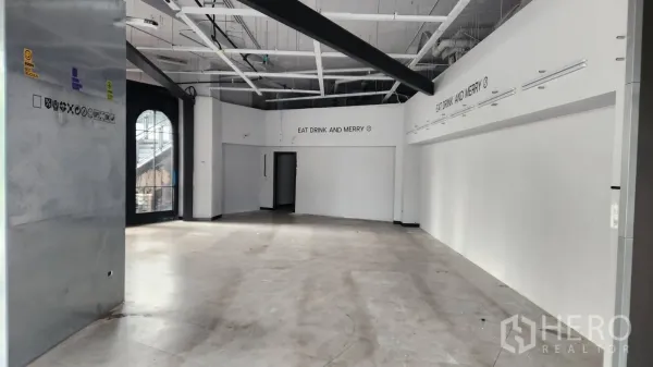 Retail Space for rent - Open-plan retail interior with a high ceiling, exposed services, concrete-look floor and an arched side door.