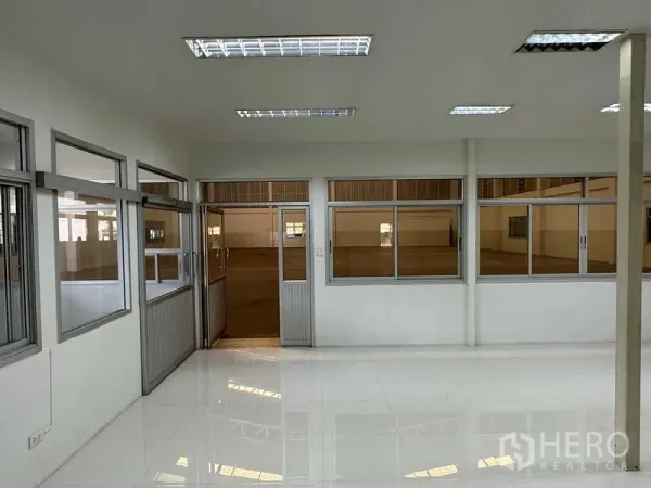 工厂 出租在Samut Prakan - 玻璃隔断办公区，白色地砖和日光灯，与生产车间相连。