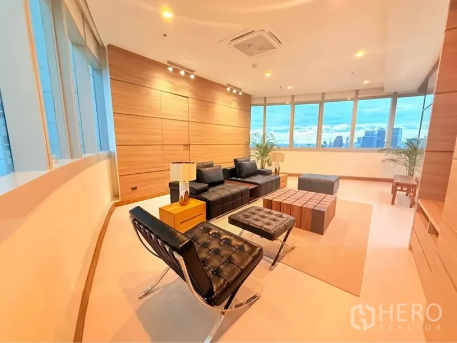 Condominium for rent or sale in Khlong Toei, Bangkok - Modern living area with spotlight ceiling, wood feature wall and black leather seating framed by wraparound windows.