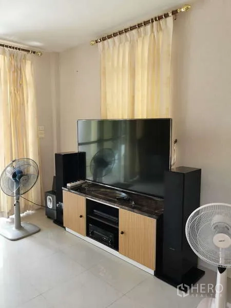 Detached House for rent - Media corner with a large flat-screen TV on a cabinet, tall speakers, and standing fans in a light-filled room.