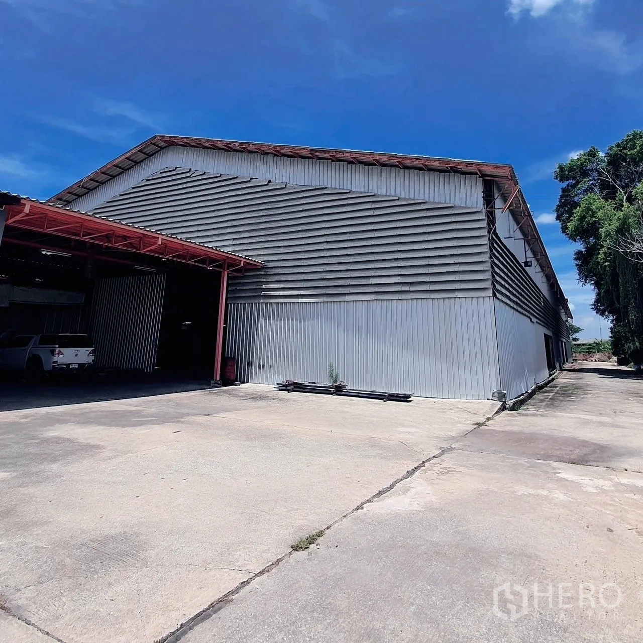 Warehouse for rent in Lam Luk Ka, Pathum Thani - Warehouse exterior with sliding doors and a broad driveway for truck parking.