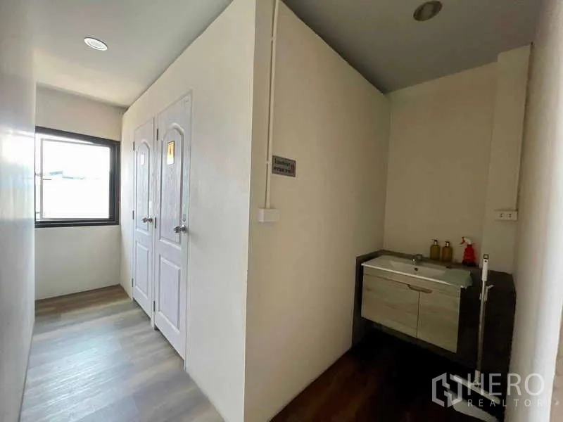 Shophouse for rent in Lat Phrao, Bangkok - Bright corridor with two restroom doors and a vanity sink beside a window.