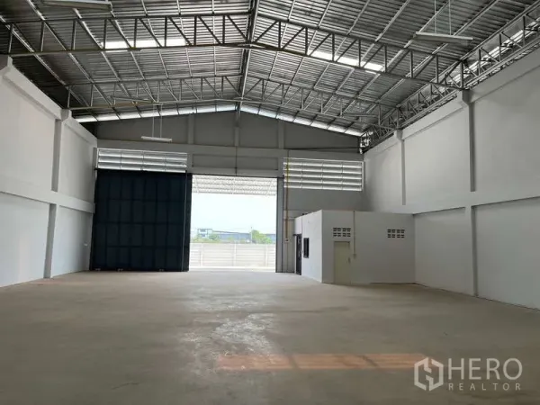 Warehouse for rent in Sam Phran, Nakhon Pathom - Spacious warehouse interior with high clear‑span steel roof, skylights, concrete floor, and wide roller shutter.