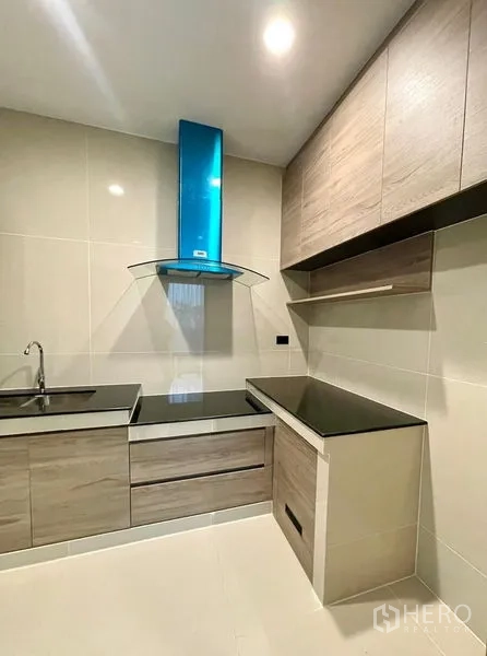 Detached House for rent in Bang Kapi, Bangkok - Compact built-in kitchen with black countertops and a blue range hood.