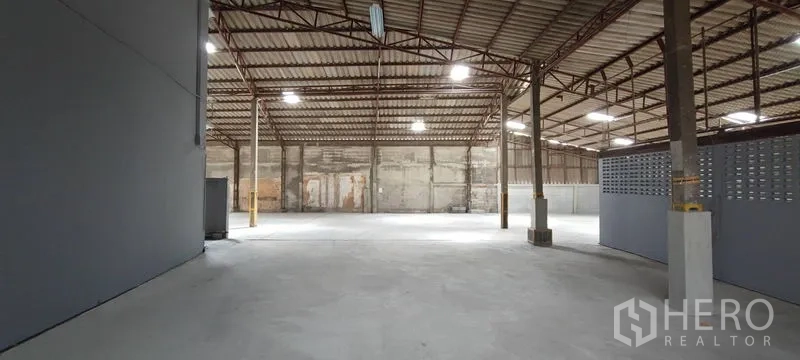 Warehouse for rent in Phra Khanong, Bangkok - Panoramic view of the warehouse floor with steel roof structure, bright lighting, and block ventilation wall.