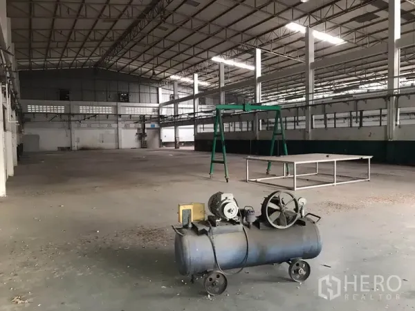 Factory for rent in Mueang Chon Buri, Chon Buri - Industrial interior showing clear-span floor with a small compressor and green gantry frame.