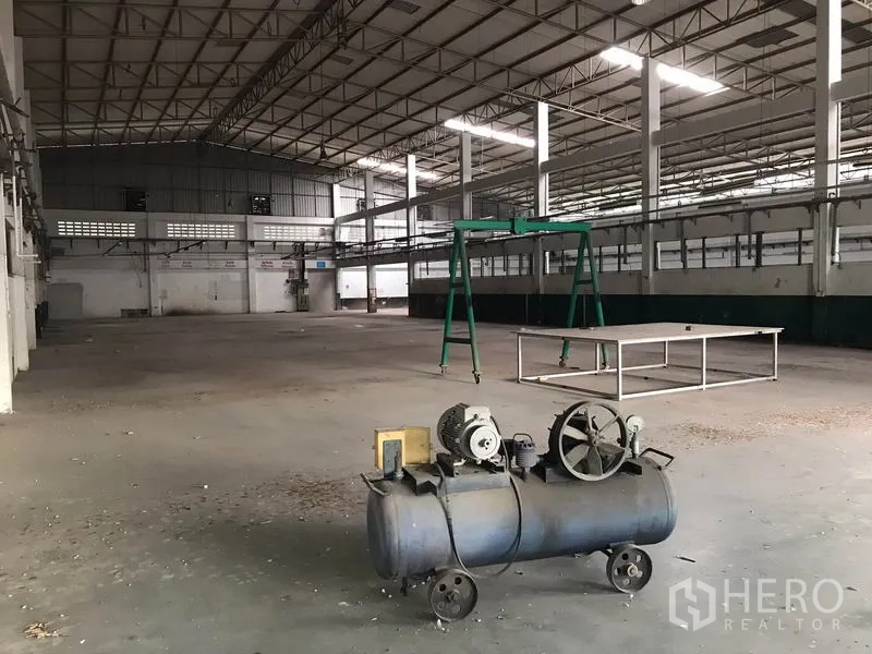 Factory for rent in Mueang Chon Buri, Chon Buri - Industrial interior showing clear-span floor with a small compressor and green gantry frame.