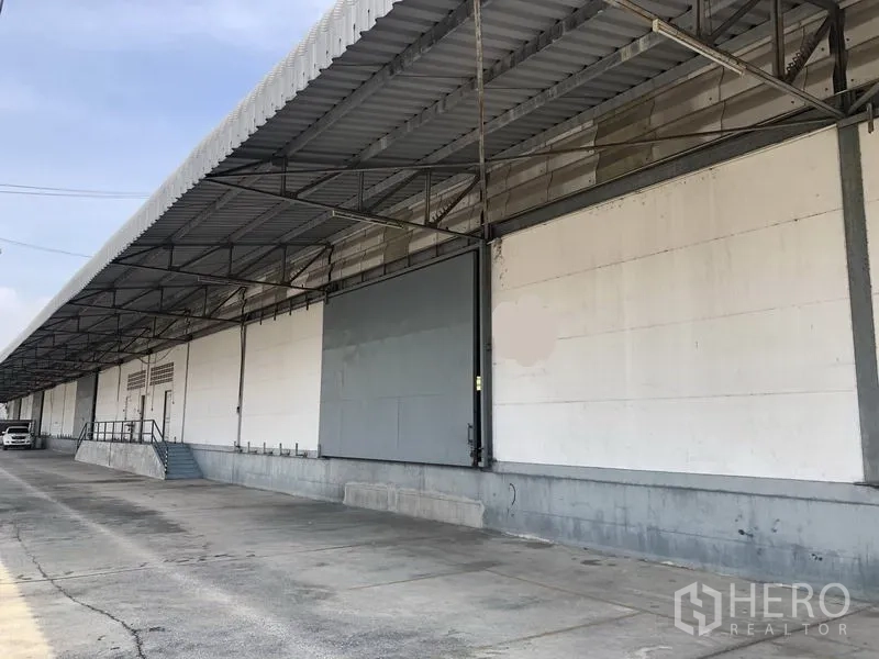 Warehouse for rent in Khlong Luang, Pathum Thani - Side view of the long covered loading bay with ramp and stairs along a wide truck lane.