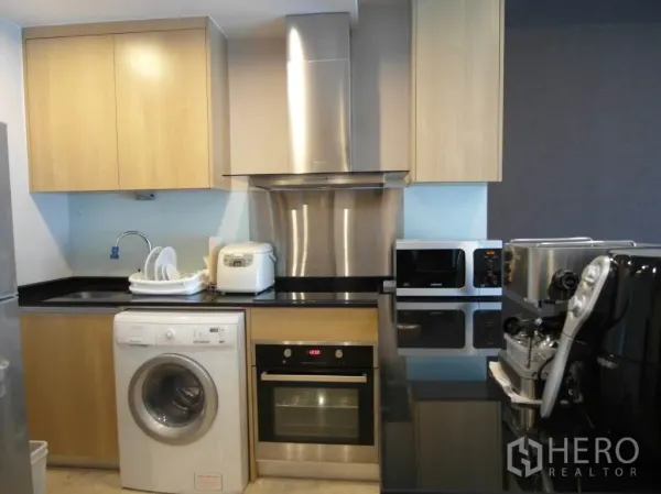 Condominium for rent or sale in Sathon, Bangkok - Fully equipped kitchen with black countertops, oven, range hood, washing machine, microwave and coffee machine.