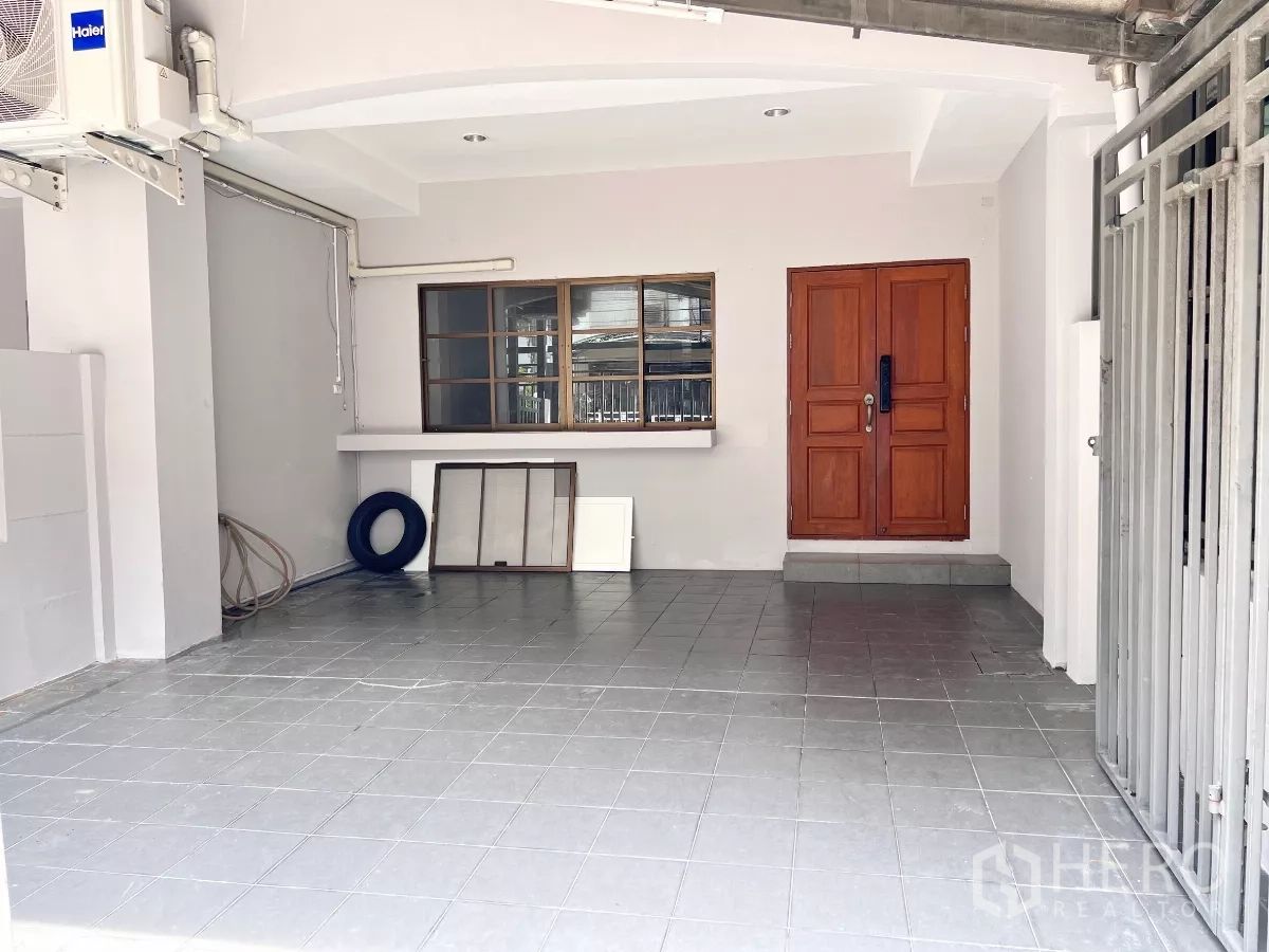 Townhouse for rent or sale in Phra Khanong, Bangkok - Ground-floor covered carport and entry with tiled floor and solid wooden front door.
