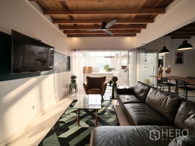 Townhouse for rent in Khlong Toei, Bangkok - Spacious living room with leather sofa, TV wall, wood-beam ceiling and sliding doors connecting to dining and kitchen.