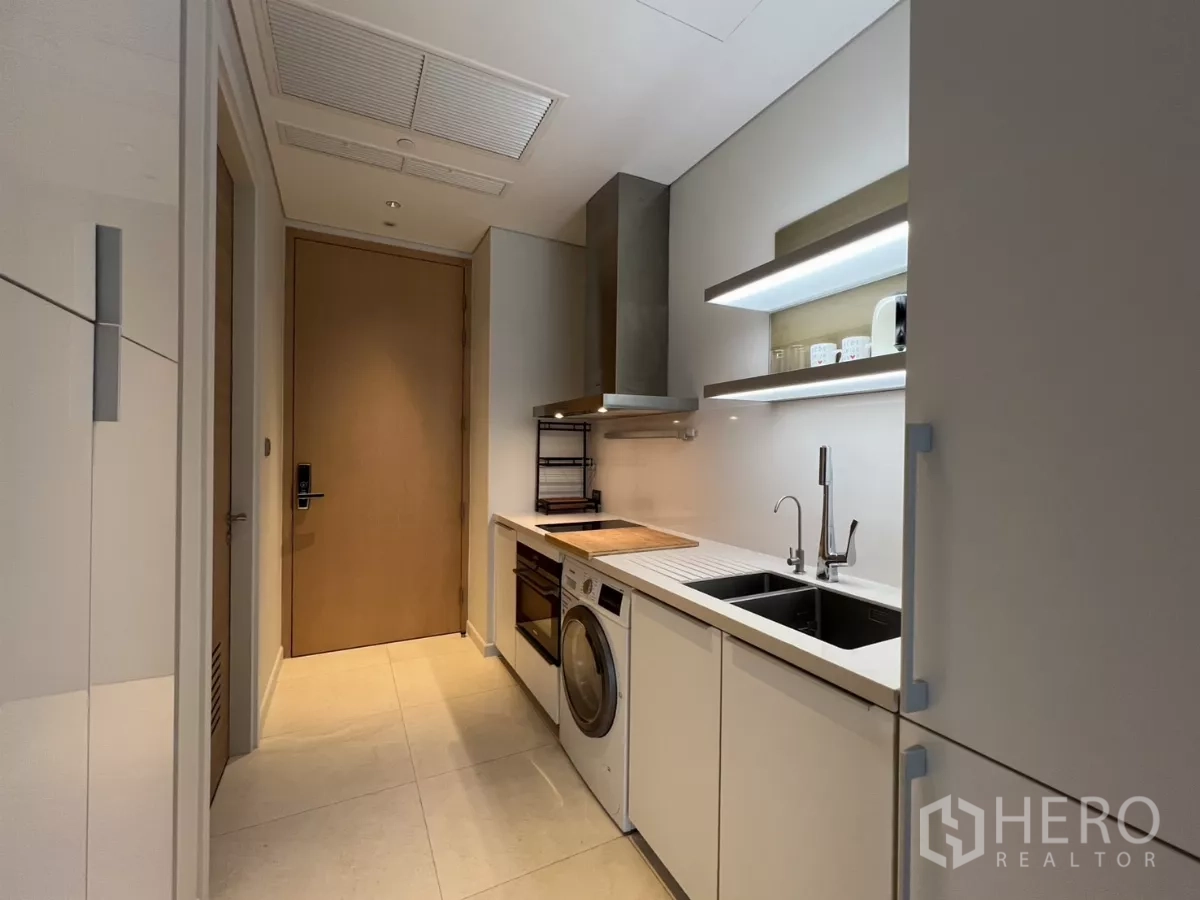 Condominium for rent in Pathum Wan, Bangkok - Corridor-style kitchen with double sink, open shelves and the main entry door.