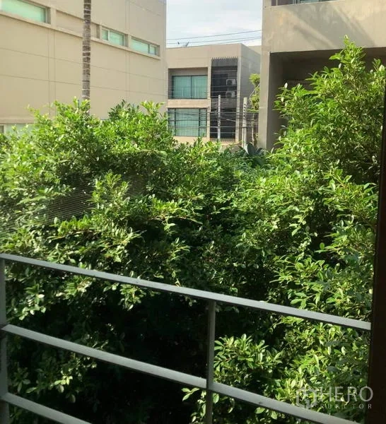 Townhouse for rent or sale in Suan Luang, Bangkok - Balcony view over lush trees toward neighboring modern low-rise buildings.