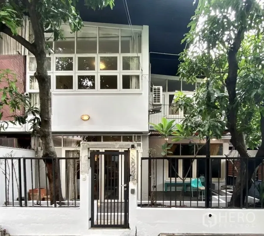 Townhouse for rent in Khlong Toei, Bangkok - Two-storey modern townhouse facade with grid windows, trees, and a black gated entrance.