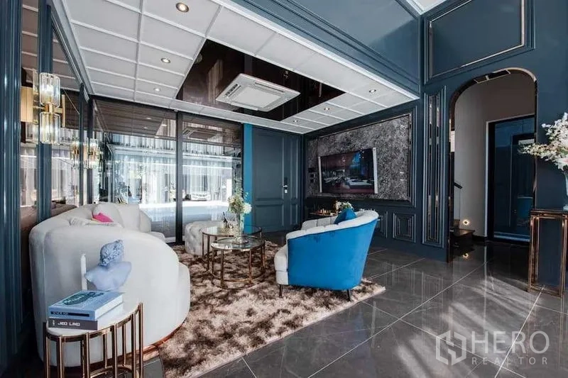 Detached House for sale in Prawet, Bangkok - Elegant living room with dark blue wall paneling, marble floors, plush sofas and a built‑in TV feature wall.