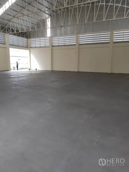 Factory for rent or sale in Mueang Samut Prakan, Samut Prakan - High-ceiling warehouse interior with steel trusses and louvered ventilation windows.