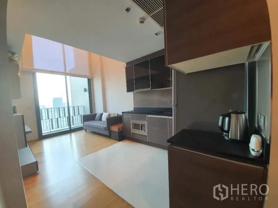Condominium for rent or sale in Khlong Toei, Bangkok - Open-plan kitchen and living room with high ceiling, wood floors, and balcony city view.