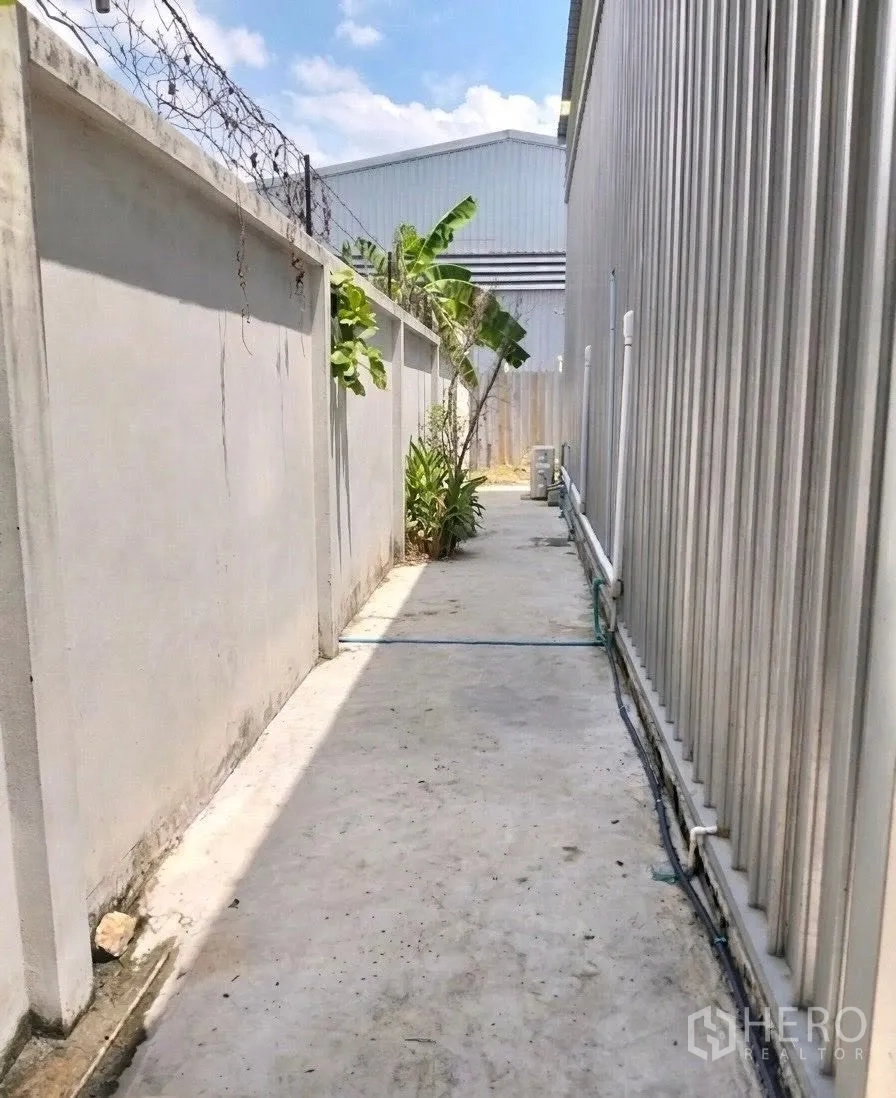 Warehouse for rent in Don Mueang, Bangkok - Rear service path with perimeter wall, security wire and exterior piping.