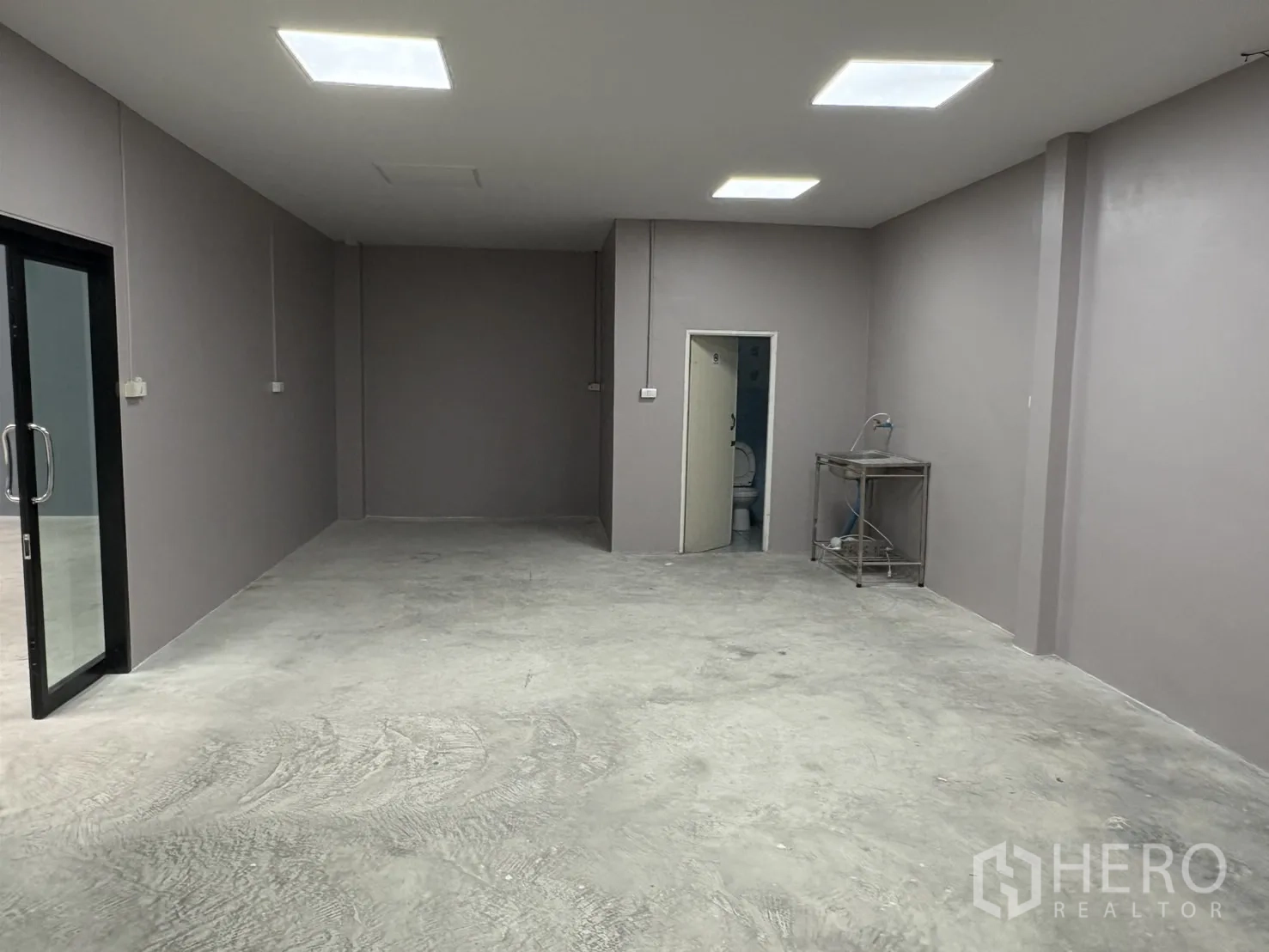 Warehouse for rent in Bang Phli, Samut Prakan - Built-in office room with glass door, bright ceiling lights, concrete floor, and access to a restroom.