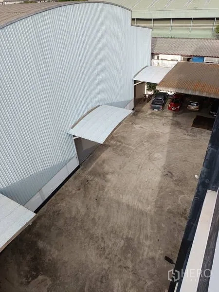 Factory for sale in Ban Phaeo, Samut Sakhon - Aerial view of side yard beside metal-clad warehouse with loading canopies and parking.