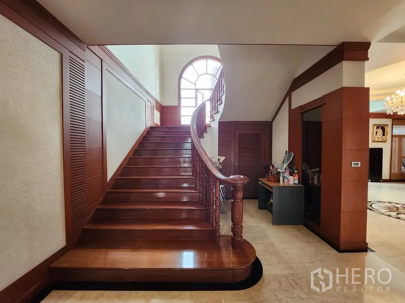 Detached House for rent in Prawet, Bangkok - Close view of the wide polished wooden staircase with classic banister and arched window.