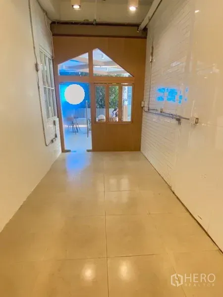 Retail Space for rent in Watthana, Bangkok - Narrow retail interior with tiled floor leading to a wood-and-glass entrance and white brick feature wall.