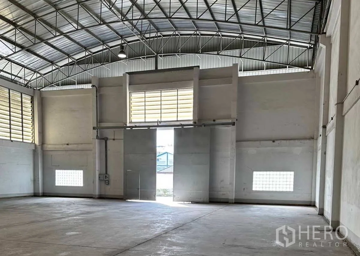 Factory for rent in Krathum Baen, Samut Sakhon - Spacious factory interior with high steel-truss roof, large sliding loading doors, and ventilation louvers.