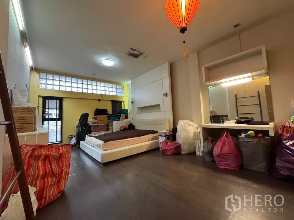Shophouse for rent in Bang Rak, Bangkok - Spacious bedroom with yellow feature wall, low platform bed, and hanging lantern.