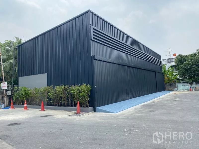 Warehouse for rent in Wang Thonglang, Bangkok - Modern black metal warehouse exterior with large sliding doors, hedge and wide driveway for truck access