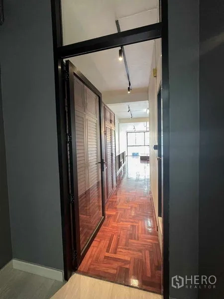 Home Office for rent in Khlong Toei, Bangkok - Hallway with glossy parquet floor and built-in wardrobes leading to a bright room.
