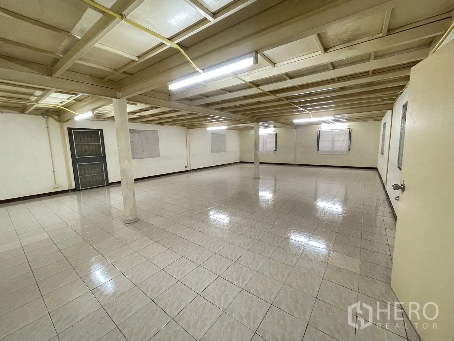 Warehouse for rent in Lat Phrao, Bangkok - Large open tiled room with low ceiling, fluorescent lights and support columns.
