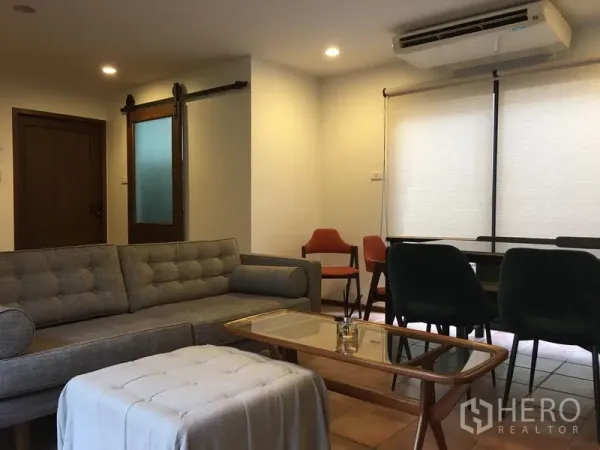联排别墅 出租在Khlong Toei, Bangkok - 客餐厅一体，灰色沙发、餐桌椅与空调。