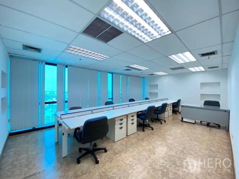 Office Space for rent - Fitted office room with long workstations, rolling chairs, ceiling lights and city-view windows.