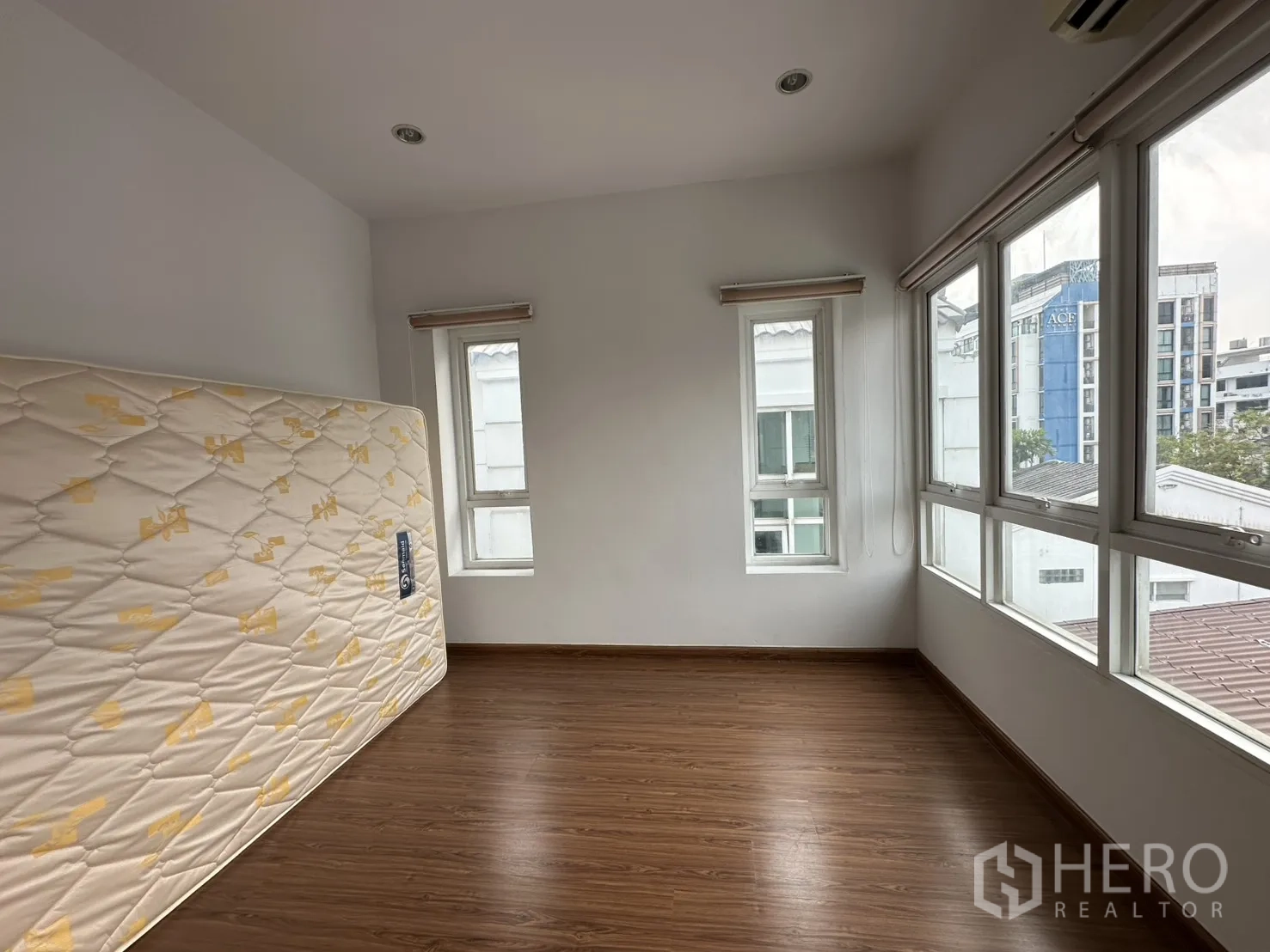 Home Office for rent in Watthana, Bangkok - Corner room with wraparound windows, wood floor and a spare mattress propped against the wall.