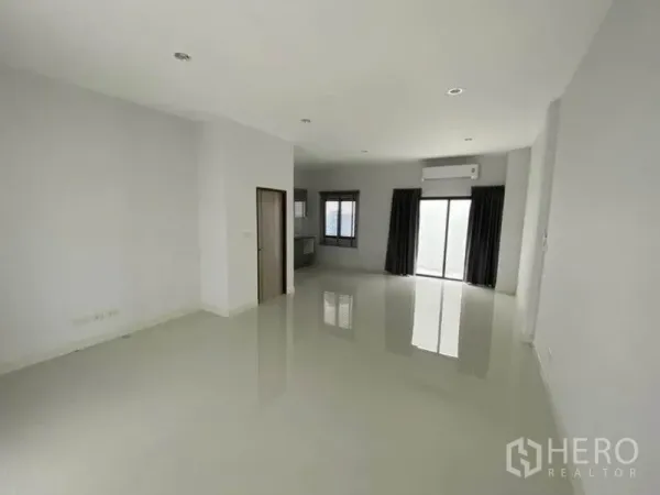 Townhouse for rent in Bang Na, Bangkok - Bright open-plan living area with glossy tile flooring, recessed lights and sliding glass doors with curtains.