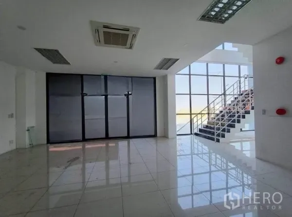 Warehouse for rent or sale in Pathum Thani - Bright lobby with floor-to-ceiling windows, tiled floors, and a glass stairway.