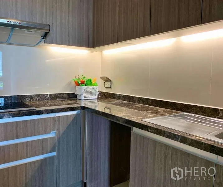 Condominium for rent - Close-up of L-shaped kitchen with marble countertop, sink, and under-cabinet lighting.