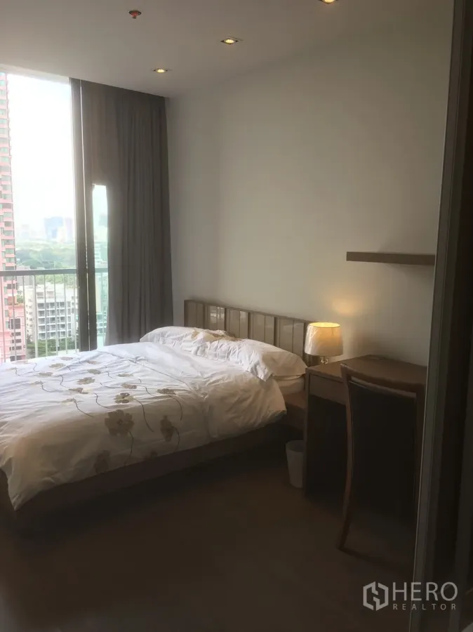 Condominium for rent or sale in Khlong Toei, Bangkok - Bright bedroom with queen bed, desk and a balcony overlooking the city skyline.