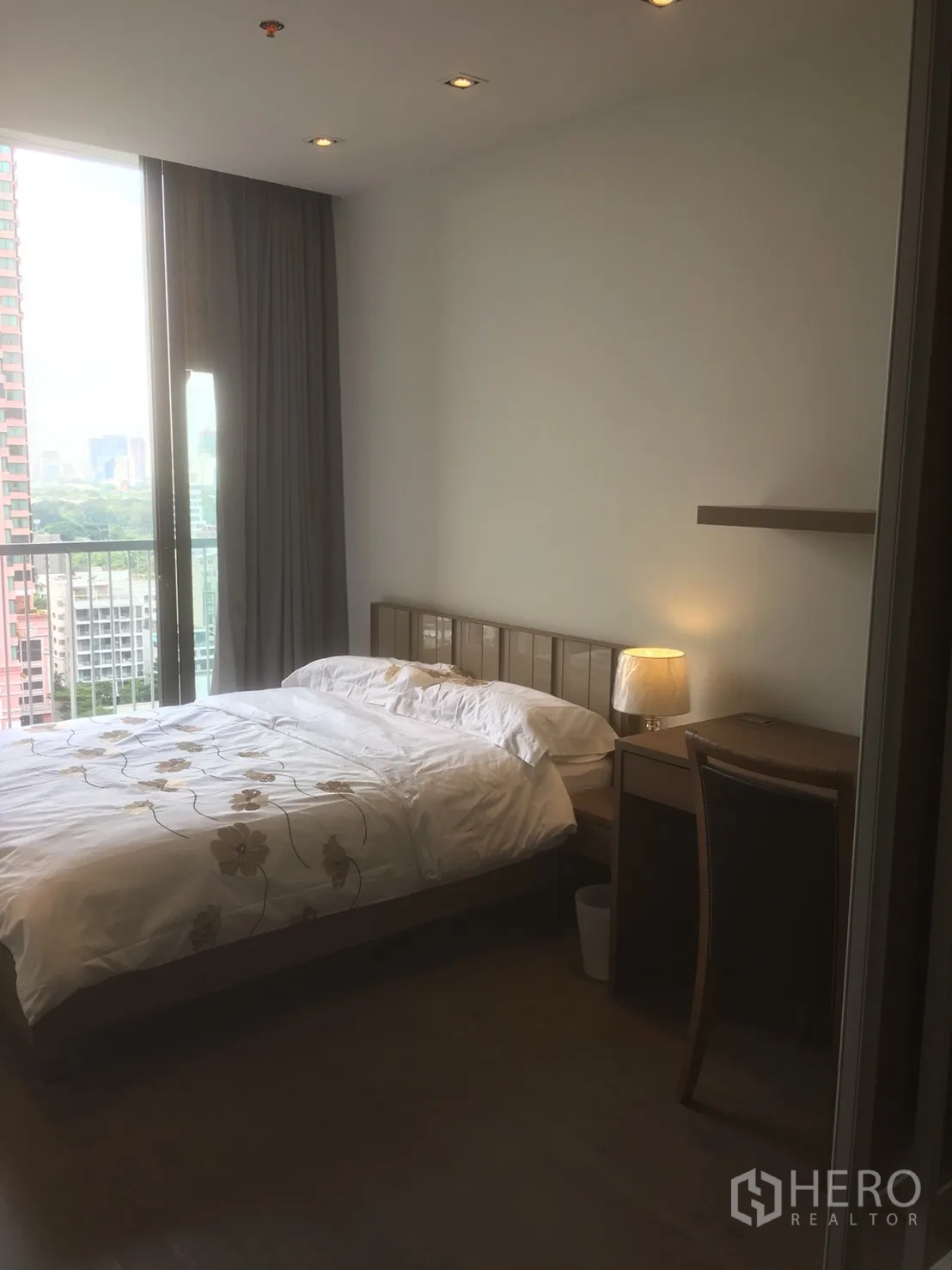 Condominium for rent or sale in Khlong Toei, Bangkok - Bright bedroom with queen bed, desk and a balcony overlooking the city skyline.