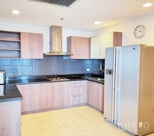 Condominium for rent in Khlong Toei, Bangkok - Modern L‑shaped kitchen with wood cabinetry, black stone countertops, range hood and a large stainless refrigerator.