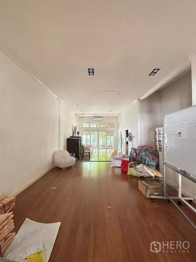 Townhouse for rent in Watthana, Bangkok - Long open room with laminate flooring, recessed ceiling lights and glass doors to a balcony.