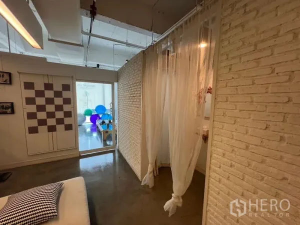 Retail Space for rent - Bright retail interior with white brick walls, sheer curtains, and polished concrete leading to a studio area with fitness balls.