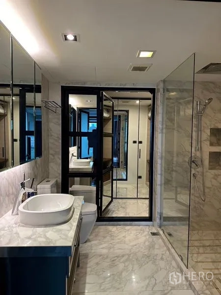 Condominium for sale in Pathum Wan, Bangkok - Marble bathroom featuring vessel sink, wide mirror and glass-enclosed walk-in shower.
