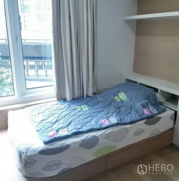 Condominium for rent in Khlong Toei, Bangkok - Cozy bedroom with a single bed, shelving and a large window with city outlook.