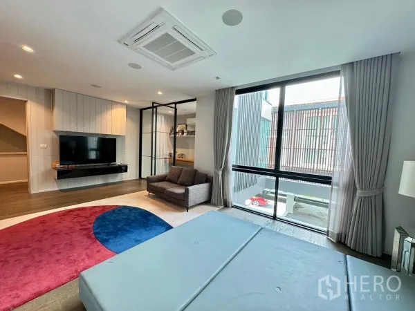 Detached House for rent or sale in Prawet, Bangkok - Family room with floor-to-ceiling windows, curtains and wall-mounted TV.