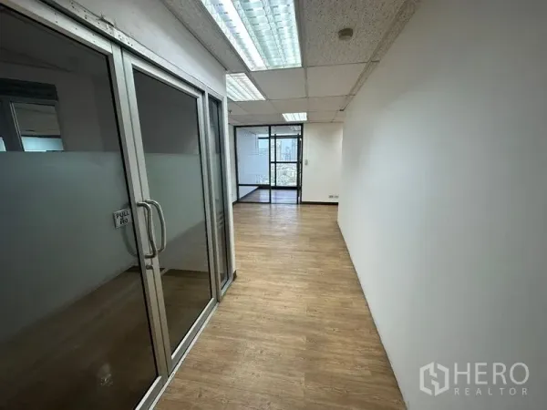 Office Space for rent - Glass-partitioned corridor with wood flooring and fluorescent ceiling lights in an office.