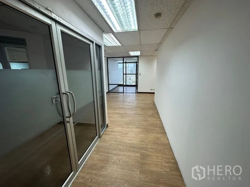 Office Space for rent - Glass-partitioned corridor with wood flooring and fluorescent ceiling lights in an office.